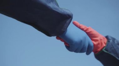 Koruyucu eldivenli iki kişiyi selamlıyorum. Yaz mevsiminde gökyüzünün arka planında yumruk tokuşturma. Covid-19 salgın yaşam tarzı, karantina toplantısı, küresel hava kirliliği.