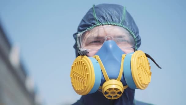 Kaukázusi férfi, védőruhában és lélegeztetőgépben. Portré munkásokról, akik a szabadban állnak a napsütéses napon radioaktív szennyezés helyett. Veszélyes emberi tevékenységek, toxikus hatás. — Stock videók