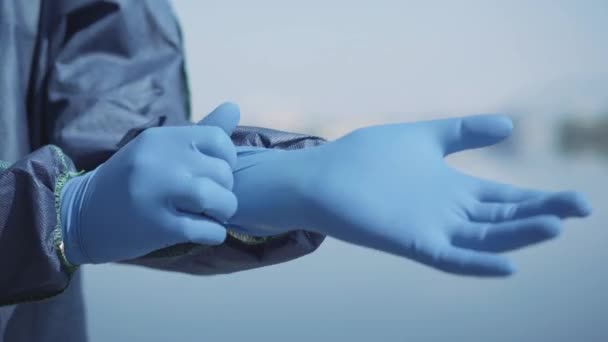 Närbild av mänsklig hand sätta på blå skyddshandske. Oigenkännlig arbetare i antiviral kostym gör sig redo att desinficera offentlig plats utomhus. Covid-19, luftföroreningar, global fara. — Stockvideo