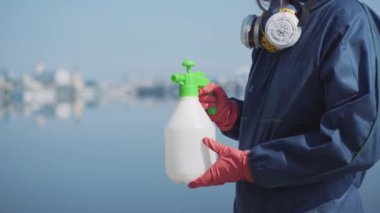 Koruyucu kimyevi kıyafetli, kimliği belirsiz bir adama kimyasal dezenfektanlı bir şişe veren tanımlanamayan bir kadın. Covid-19 'da işçiler güneşli bahar ya da yaz günlerinde açık havayı dezenfekte ediyorlar..