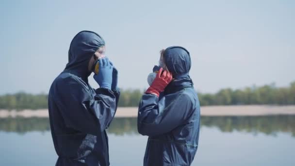 Due specialisti caucasici in tute chimiche e occhiali protettivi che si mettono i respiratori e danno il cinque. Vista laterale dei lavoratori fiduciosi che disinfettano le strade su Covid-19 o inquinamento chimico — Video Stock