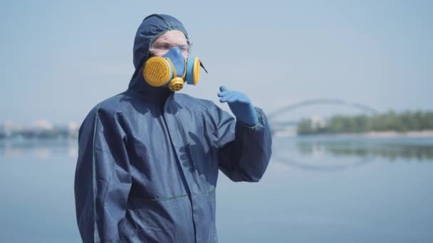Eine unkenntliche Frau im Chemikalienanzug kommt mit Atemschutzmaske und Schutzbrille zu einem jungen Mann im Freien. Junges kaukasisches Paar beim Umarmen. Radioaktive Luftverschmutzung, Covid-19-Pandemie. — Stockvideo
