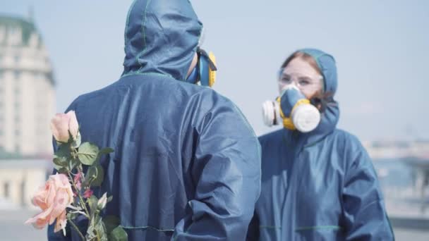 Datum för älskande kaukasiska par på Covid-19 pandemi eller radioaktiv kemisk förorening. Fokus förändringar från bukett av rosor till nöjd ansikte ung söt kvinna luktar blommor genom respirator. — Stockvideo
