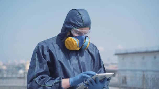 Portret van een serieuze man in een chemisch pak die buiten tabletten gebruikt. Jong overtuigd Kaukasische specialist registreert gegevens van radioactieve luchtverontreiniging. Lifestyle op Covid-19 pandemie. Coronavirus, gevaar. — Stockvideo