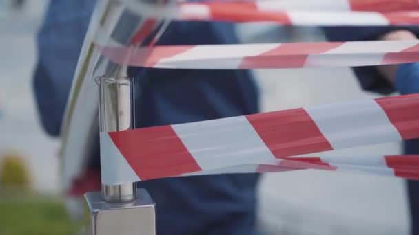 La caméra se déplace le long de la bande d'avertissement tendue par des personnes méconnaissables en combinaison chimique et gants de protection. Travailleurs inconnus faisant barrière avec du ruban adhésif rouge et blanc. Covid-19, pollution atmosphérique . — Video