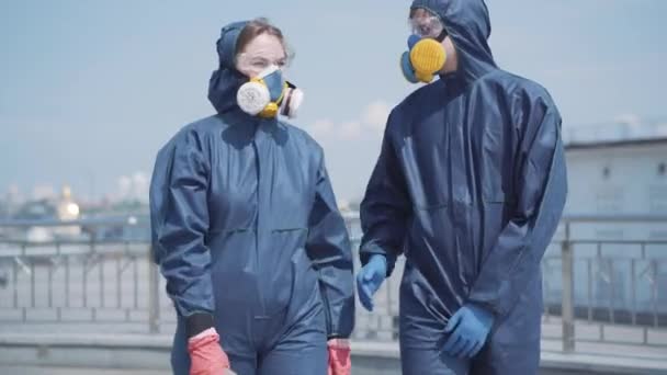 Pareja joven saliendo al aire libre en trajes químicos y respiradores. Retrato de una mujer hermosa y un hombre guapo paseando por la calle de la ciudad y hablando. 9º Covid-19, contaminación atmosférica, riesgo biológico, estilo de vida . — Vídeos de Stock