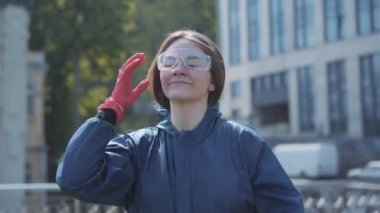 Neşeli esmer kadın solunum cihazını, gözlüğünü çıkarıyor ve fermuarını açıyor. Güneşli bir günde karantinanın sonunda eğlenen neşeli beyaz kız portresi. Covid-19 yaşam tarzı.
