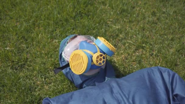 Primer plano del hombre en respirador acostado sobre hierba verde de verano y mirando hacia arriba sosteniendo la mano en la frente. Retrato de un joven caucásico relajado disfrutando de un soleado día de primavera al aire libre. Contaminación atmosférica, Covid-19 . — Vídeos de Stock