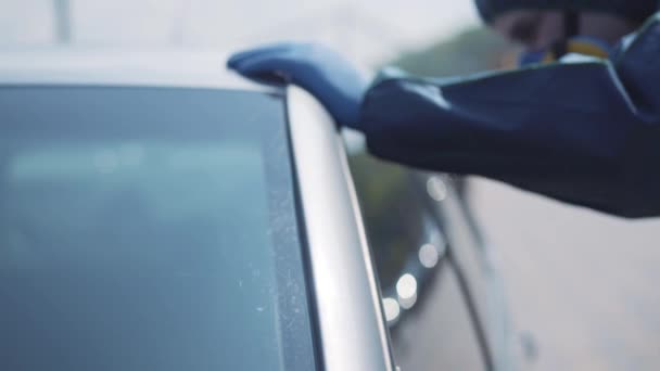 Biały mężczyzna w respiratorze i niebieskim kombinezonie, patrzący w srebrny samochód przez boczne okno. Zbliżenie niewyraźnego pracownika konsultującego się z kierowcami na drodze miejskiej. Kwarantanna Covid-19, zanieczyszczenie radioaktywne. — Wideo stockowe
