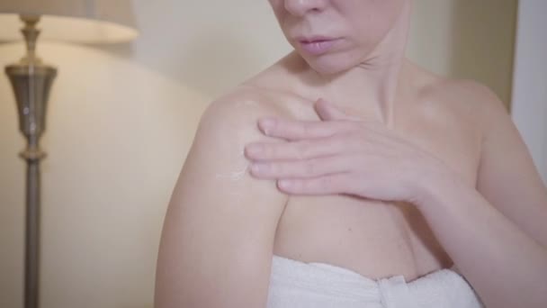 Superbe femme blanche qui applique une crème anti-âge pour le corps. Femme adulte méconnaissable en serviette blanche prenant soin de la peau et souriant. Beauté, soins, rajeunissement, style de vie . — Video