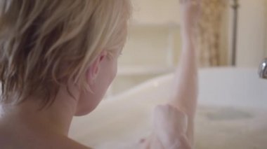 Sarışın bir kadının jiletle bacaklarını tıraş edişinin arkası. Genç beyaz kadın banyoda cesetle ilgileniyor. Omzundan vuruluyor. Yaşam tarzı, güzellik, hijyen, tüy dökücü..