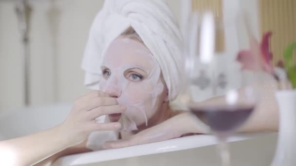 Happy woman taking off rejuvenating face mask and smiling at camera. Portrait of charming Caucasian adult lady enjoying beauty procedure in bathroom. Lifestyle, beauty, femininity, pampering. — Stock Video