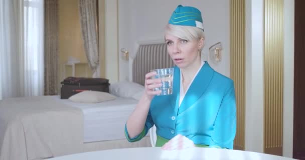 Mooie blanke vrouw die water drinkt in haar hotelkamer. Portret van een zelfverzekerde vrouwelijke stewardess in blauw uniform. Luchtvaart, elegantie, levensstijl. Cinema 4k ProRes Hoofdkwartier. — Stockvideo