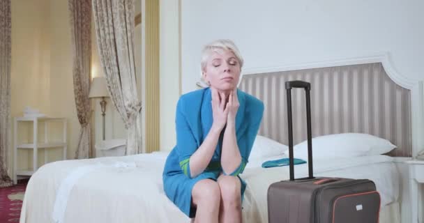 穿着空姐制服的疲惫的白人金发女人坐在酒店房间的床上的画像。飞行困难后,空姐放松得精疲力竭.工作过度，航空，生活方式。Cinema 4k ProRes HQ — 图库视频影像