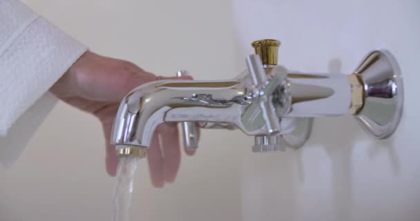 Gros plan de la main blanche femelle allumant l'eau et vérifiant la température avec les doigts. Femme méconnaissable préparant le bain. Hygiène, baignade, soins. Siège social Cinema 4k ProRes . — Video