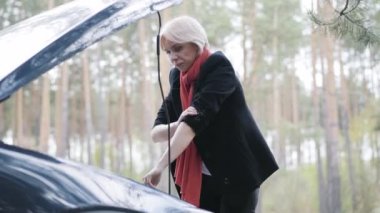 Ciddi sarışın kadın kollarını sıvayıp araba kaputunda motor arızasını düzeltiyor. Kenar mahallelerde araba kazası geçiren kendine güvenen beyaz kadın sürücünün portresi. Sorun, sorun, turizm.