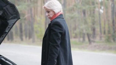 Açık kapüşonlu kırık bir arabada dolaşan belirsiz sarışın bir kadın. Banliyö yolunda ingiliz anahtarı olan beyaz kadın portresi. Araç arızası, sorun.