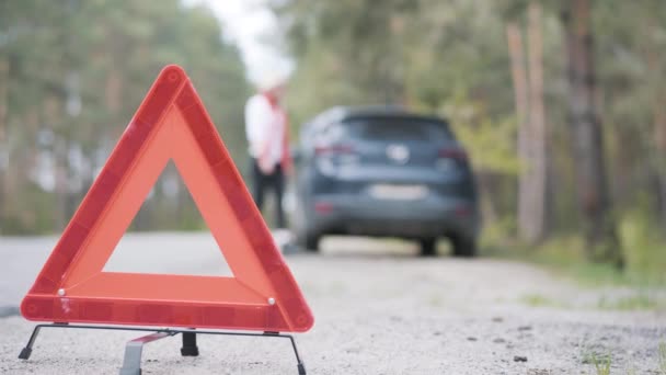Close-up of emergency stop sign on suburban road with blurred confident Caucasian woman opening car trunk at the background. Breakage of automobile on countryside highway. — Stock Video