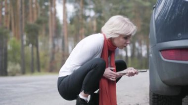 Kırsal yolda tekerlek vidalarını sıkmaya odaklanmış güzel bir kadın. Banliyö otobanında araba arızasını tamir eden zarif beyaz kadın portresi. Yaşam tarzı, seyahat, sorun, beceri.