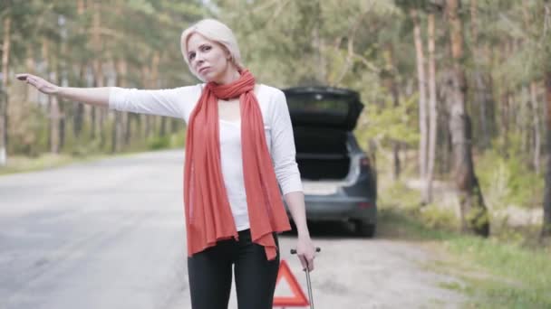 Portrait d'une jolie femme blonde avec clé à molette en auto-stop devant une voiture cassée au tronc ouvert. Belle jeune femme caucasienne besoin d'aide sur la route de banlieue. Répartition, accident, mode de vie . — Video