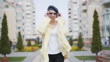 Kendine güvenen güzel sarışın kadın yürüyor ve güneş gözlüğünü çıkarıyor. Şehrimizde güneşli bir bahar gününde açık havada gezen zarif beyaz kadın portresi. Özgüven, zarafet, yaşam tarzı.