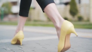 Kamera, sarı yüksek topuklu ince beyaz kadın bacaklarını kaldırımda yürürken takip ediyor. Zarif ayakkabılarla tanınmayan ince kadınların basamakları. Güzellik, moda, yaşam tarzı.