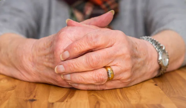 Mãos apertadas de uma mulher aposentada descansando em uma mesa . — Fotografia de Stock