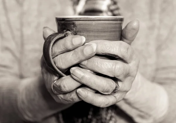 Sıcak bir içecek holding yaşlı kadının eller. Tek renkli. — Stok fotoğraf