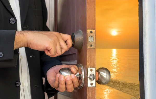 Бизнесмен открывает дверь ключом к закату с видом на море — стоковое фото