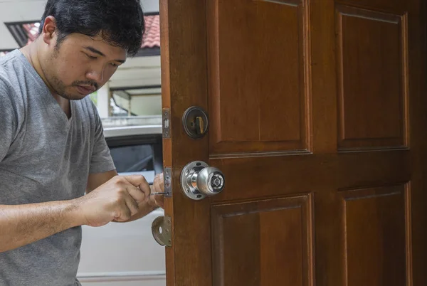 Слюсар фіксує срібну ручку викруткою на дерев'яних дверях — стокове фото