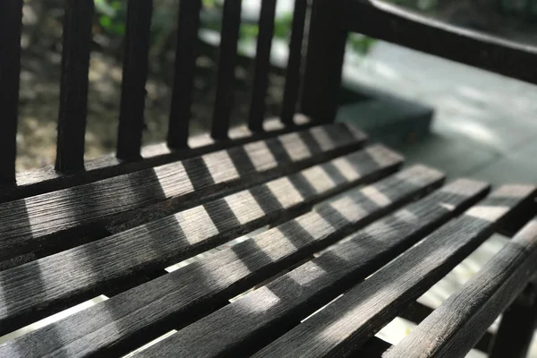 Banc en bois brun foncé de jardin avec lumière du jour et ombre — Photo