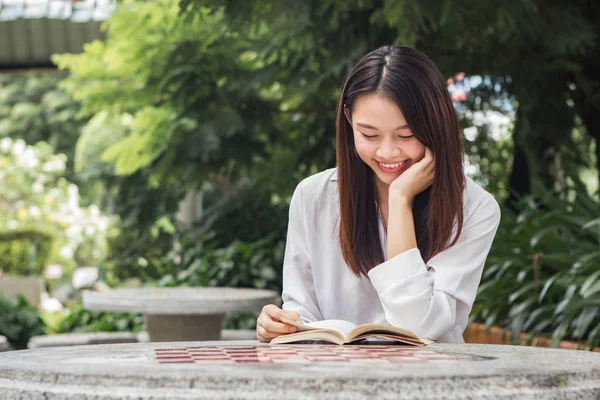Asiatisk kvinna läser bok på bordet inuti naturparken — Stockfoto
