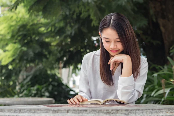 Asiatisk kvinna läser bok på bordet inuti naturparken — Stockfoto
