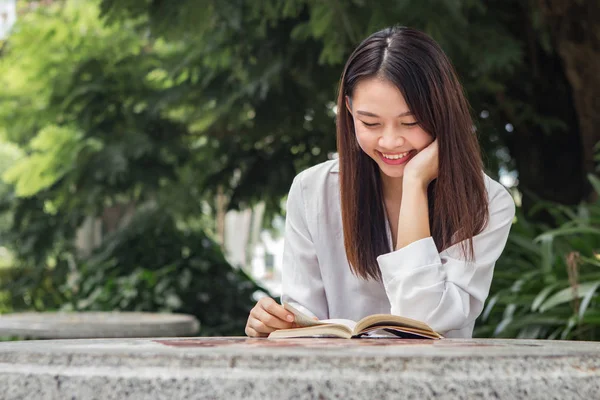 Asian woman reading book on the table inside natural park Stock Photo