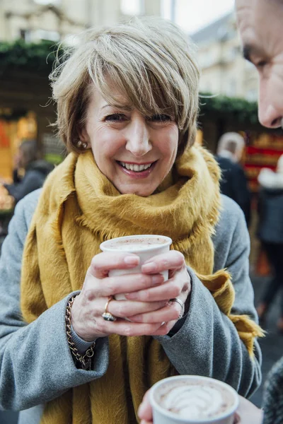 Oudere vrouw warme chocolademelk drinken op kerstmarkt — Stockfoto