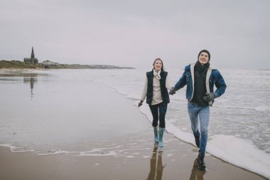 Genç çift bir kış plaj boyunca yürüyüş