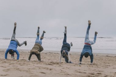 Friends Doing Handstands On A Winter Beach clipart