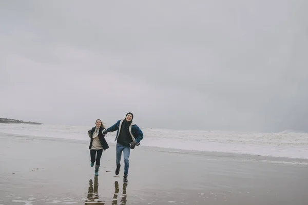 Um jovem casal correr ao longo de uma praia de inverno — Fotografia de Stock