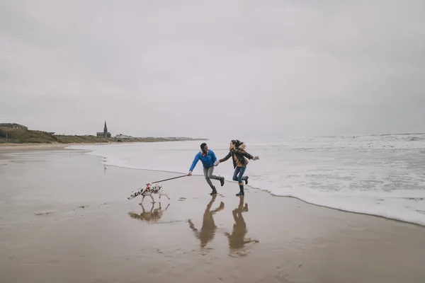 Jovem casal correr ao longo inverno praia com seu cão — Fotografia de Stock