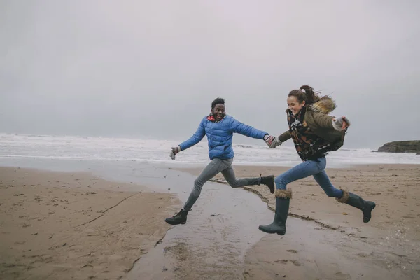 Casal jovem pular ao longo de uma praia de inverno — Fotografia de Stock