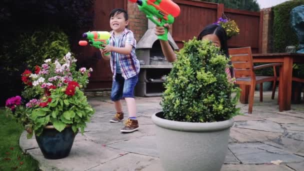 彼らは 水鉄砲を持っていると 庭の植木鉢の後ろに隠れているの兄弟家族と庭で戦う — ストック動画