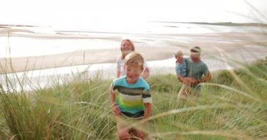 Ağır çekim shot gülüyor ve sahilde kum dune kadar çalıştırırken gülümseyen bir ailenin.