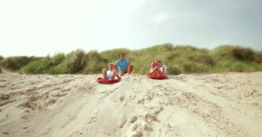 Yavaş hareket iki kardeş bir kumul kum panoları, otururken aşağı itti olmasına bir rekabet olan bir kadeh. Bir çocuk kum tahtasından düşer ve diğer altına yapar.