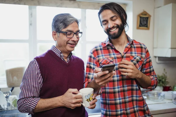 中年男子在他的智能手机上显示他成熟的父亲的东西 他拿着一杯茶 — 图库照片