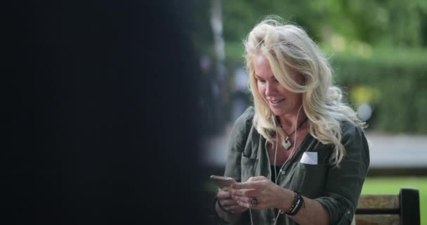 Una Mujer Sentada Banco Del Parque Usando Auriculares Para Escuchar — Vídeos de Stock