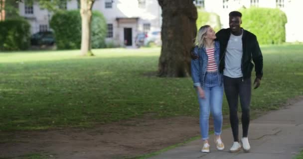 一个女人和一个男人在人行道上走过一个公园 他们一边走一边互相拥抱 一边说话笑 — 图库视频影像