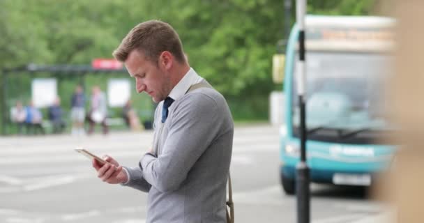 彼の携帯電話を見てタイプする街の通りに立っているビジネスマン 彼はその後 彼の周りで何が起こっているか見て回る — ストック動画