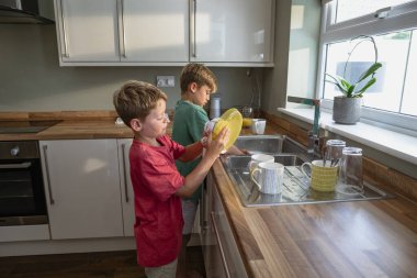 Bulaşıkları yıkayan iki genç kardeşin yan görüntüsü..