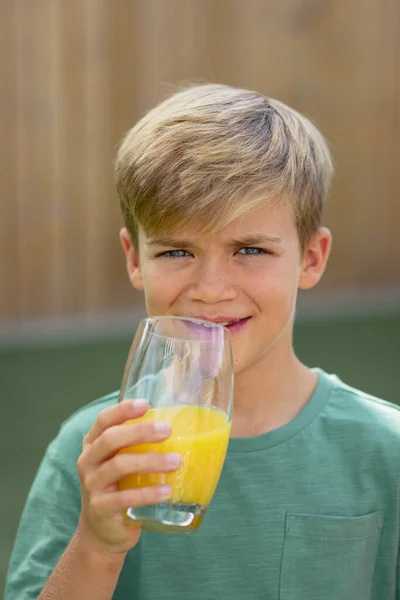 カメラを見て微笑む少年の正面からの眺めは オレンジジュースのグラスを持っている — ストック写真