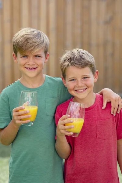 カメラを見て笑っている2人の少年の正面からの眺め 彼らはオレンジジュースのガラスを持っている — ストック写真